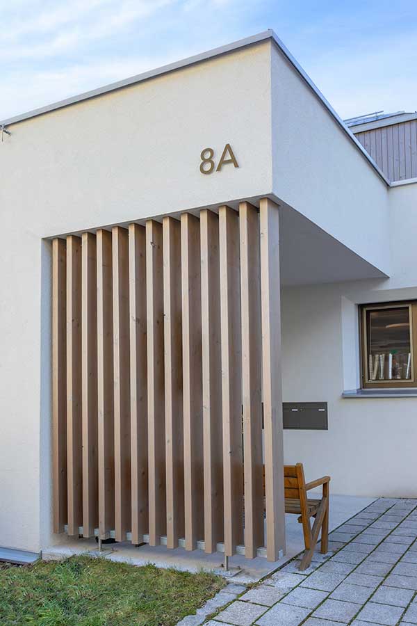 Minimalistisches Gebäude mit weißer Fassade, Holzlamellen und der Hausnummer 8A neben dem Eingang. © SARA BUBNA photography
