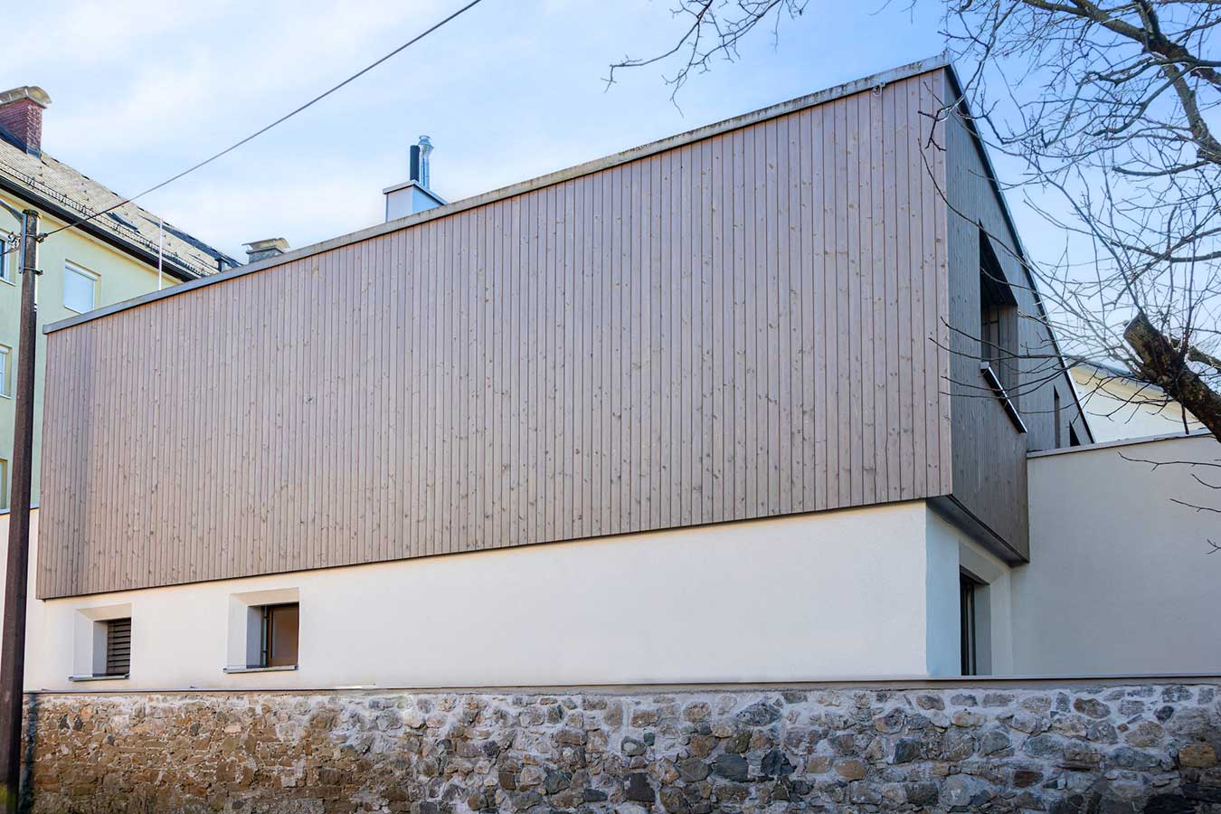 Moderner Bau mit weißem Untergeschoss und Holzfassade oben, schlichtem Design und schrägem Dach. © SARA BUBNA photography