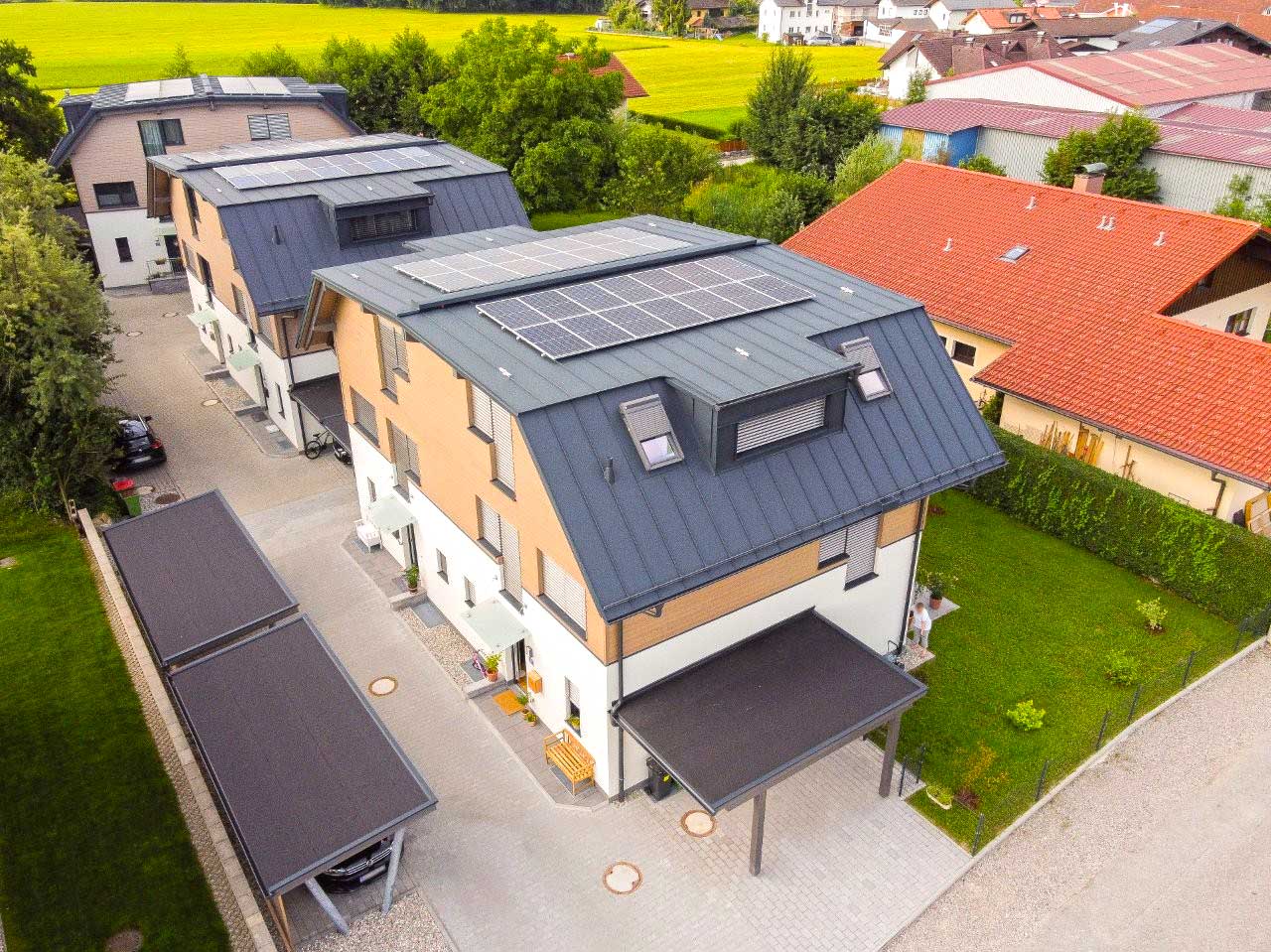 Moderne Wohnsiedlung mit mehrstöckigen Häusern, schrägen Metalldächern, Holzverkleidung, weißen Fassaden, kleinen Gärten und Sitzbereichen