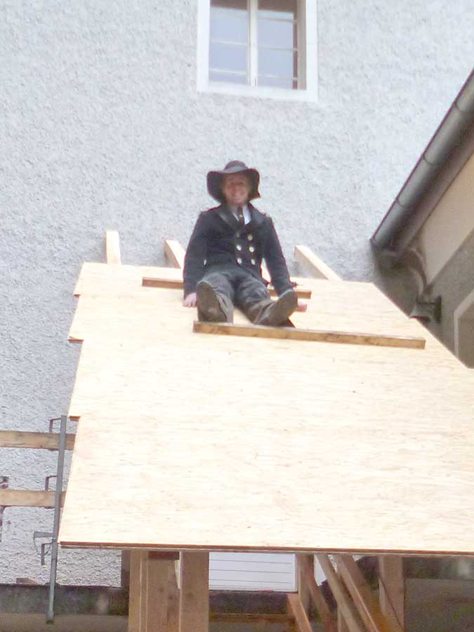 Wandergeselle in typischer Kleidung sitzend auf einem Holzdach