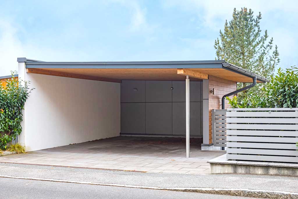 Überdachter Carport mit Holzdecke, weißer Wand und seitlichem Lamellenzaun © SARA BUBNA photography