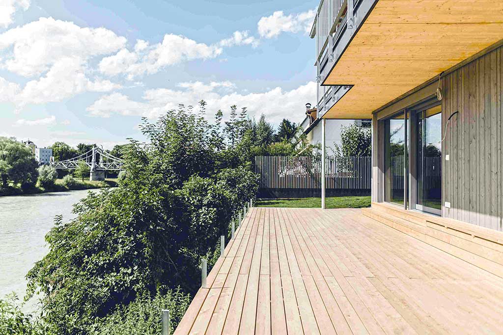 Modernes Haus mit großer Holzterrasse und Blick auf den Fluss Salzach, im Hintergrund Brücke